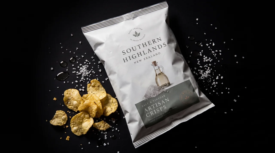 Artisan crisps packaging — studio still on dark backdrop with scattered chips and salt